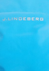 Modrá tkanina s hladkou texturou, na horní části s raženým stříbrným logem "J. LINDEBERG".