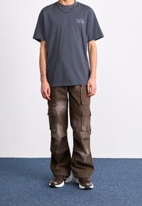 Grå bomullströja med lila Nike-logga och löst sittande bruna cargobyxor med flera fickor, bärs med kraftiga sneakers. Avslappnat outfit.