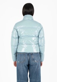 Lichtblauwe, glanzende pufferjack met een hoge kraag, gestikt design en effen kleur. Gecombineerd met high-waisted denim jeans.