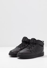 Baskets noires montantes en simili cuir avec un embout perforé, un laçage et une sangle à boucle au niveau de la cheville.