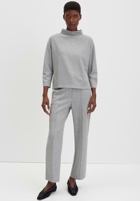 Grijze sweatshirt met een hoge kraag, lange mouwen; gecombineerd met bijpassende grijze broek met verticale naden. Zwarte flats met studs.