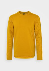 Camicia a maniche lunghe gialla senape, con maniche testurizzate, scollatura rotonda e un logo discreto sul braccio sinistro. Finitura in tessuto liscia.