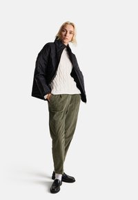 Černá prošívaná bunda, bílý texturovaný svetr a olivové kordové kalhoty. Černé loafers, slim-fit s záhyby, nošeno neformálně.