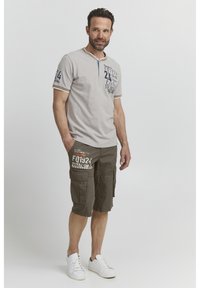 Grå kortærmet polo med blå accenter og trykt tekst, parret med khaki cargo shorts med forlommer. Hvide sneakers fuldender looket.