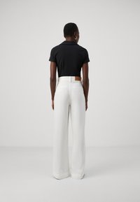 Zwarte polo-shirt met korte mouwen, gecombineerd met hooggepaste, brede witte broeken met een tan leren patch aan de achterkant.