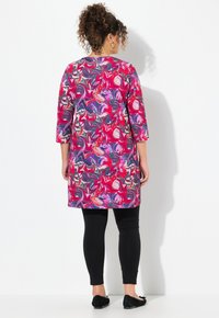 Kleurrijke tuniek met een draaiend patroon van roze, paars en blauw. Gepaard met zwarte leggings en platte schoenen. Driekwartmouwen.
