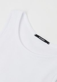Weißes, geripptes Tanktop mit rundem Ausschnitt und einem schwarzen Etikett, das innen am Kragen angenäht ist und "TEZENIS" auf weißem Hintergrund zeigt.