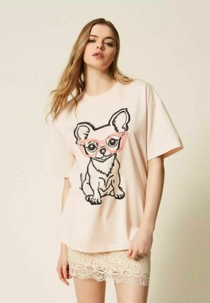 Donna che indossa una maglietta rosa pallido oversize con un grande cane dei cartoni animati con occhiali rosa, abbinata a una gonna beige in pizzo.