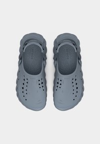 Ζευγάρι γκρι υποδη μάτων τύπου clog με οπές αερισμού και ρυθμιζόμενα λουράκια στη φτέρνα, που φαίνεται από ψηλά πάνω σε ανοιχτό φόντο.