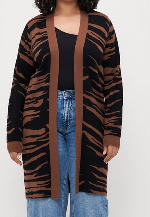 Personne portant un long cardigan noir et marron à rayures tigre par-dessus un top noir et un jean bleu taille haute.