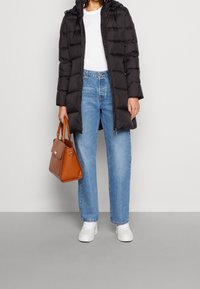 Doudoune noire avec capuche, associée à un jean large bleu clair. Des baskets blanches et un sac à main structuré marron complètent la tenue.