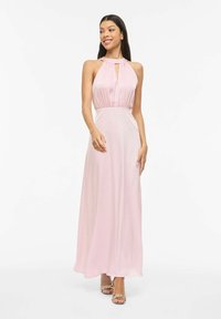 Šviesiai rožinė maxi suknelė su halterio iškirpte, surinkta medžiaga liemenyje ir raktelio formos iškirpimu. Lygus, gaivinantis audinys krenta iki grindų.