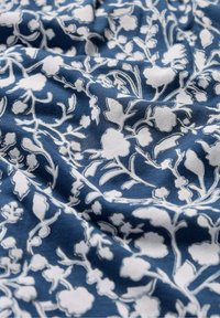 Tessuto stampato con disegni floreali bianchi su uno sfondo blu scuro, caratterizzato da dettagli intricati e una texture liscia.