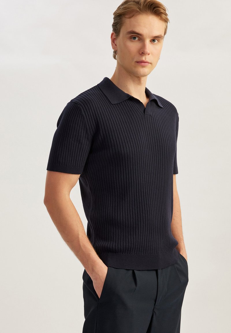 Mörk marinblå ribbad polo med korta ärmar och klassisk krage. Har en figurnära silhuett och jämn textur.