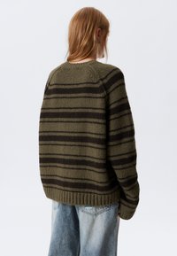 Grønn og svart stripete genser, strikket tekstur, oversized passform, ribbestrikket kant, rund hals, brukt sammen med lyseblå slitte jeans.