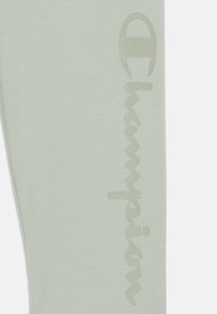 Leggings vert clair en tissu doux présentant un grand logo "Champion" ton sur ton sur le côté avec une texture légèrement en relief.