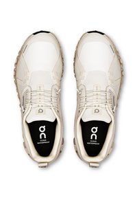 Chaussures de sport imperméables de couleur claire avec un haut en mesh texturé, une semelle en caoutchouc et un logo bien visible sur la semelle intérieure. Présente un design minimaliste.