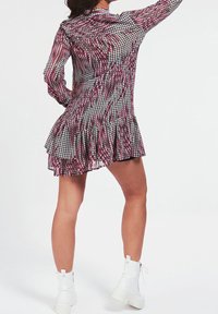 Vestido corto de tela transparente con un patrón de pata de gallo en tonos rosa, negro y blanco, con dobladillo con volantes y mangas largas. Botas blancas visibles.