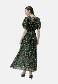 Maxikleid aus durchsichtigem schwarzem Stoff mit gelben Blumen- und grünen Blattmustern, mit schwingenden Ärmeln und tailliertem Schnitt, mit einem Bindeband im Rücken.