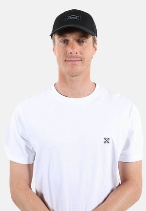 Homme portant une casquette noire avec le logo « Oxbow » et un T-shirt blanc uni avec un petit motif brodé noir sur la poitrine.