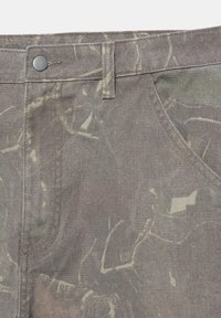 Közeli kép barna terepmintás szövetnadrágról, amelyen gomb, övhurkok és ferdén álló elülső zseb látható.