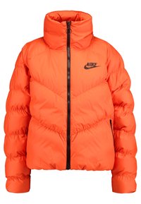 Nike puffer jacket in bright orange, featuring a high collar, front zipper, and chevron stitching pattern, with a black logo on the chest.