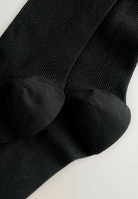 Schwarze Socken mit gerippter Textur, ausgestattet mit verstärkten Zehen- und Fersenbereichen. Weich und einheitlich in der Farbe mit einer glatten Oberfläche.