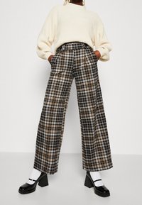 Breda byxor med rutigt mönster i brunt, svart och vitt; med hög midja, sidofickor och en mjuk tygkvalitet.