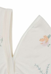 Tissu en coton blanc avec des oiseaux brodés pastel et des accents botaniques ; il présente une fermeture éclair le long de la couture pour un enfilage facile.