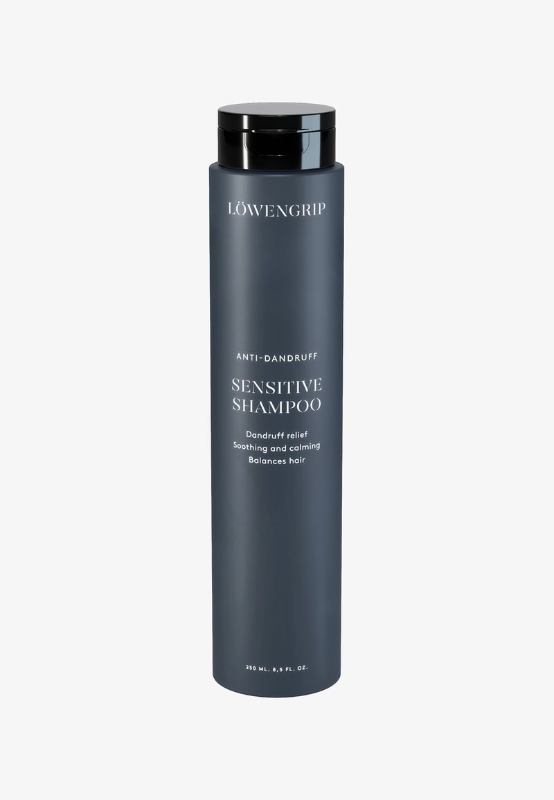 Donkergrijze, cilindervormige shampoofles met een zwarte dop. Tekst in het wit die "Anti-Dandruff" en "Sensitieve Shampoo" aangeeft. Inhoud van 250 ml.