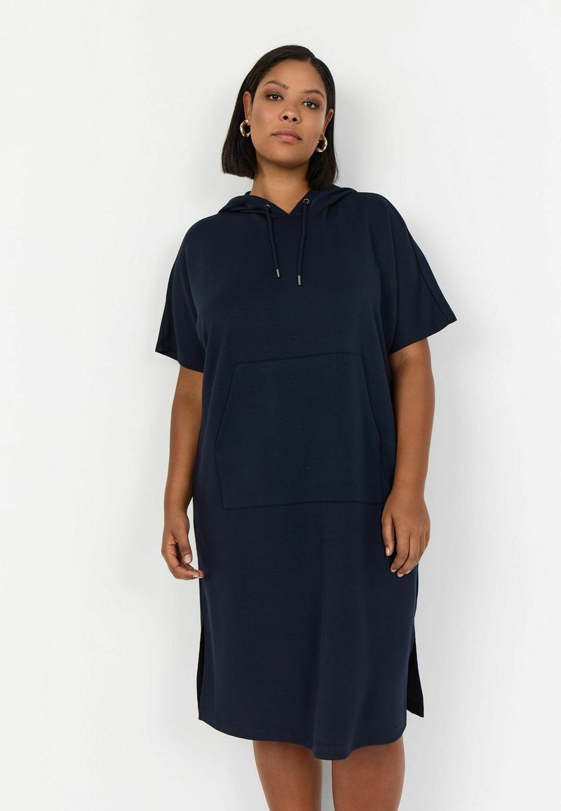 Vestido con capucha en color marino, fabricado en un tejido suave, que presenta un bolsillo delantero, mangas cortas, aberturas laterales y un corte holgado.