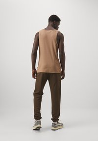 Top a righe marroni in cotone abbinato a pantaloni jogger marroni scuri, con polsini elasticizzati e sneaker grigie con accenti di crema e nero.