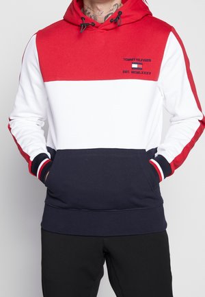 Haut à capuche coloré en blocs rouge, blanc et marine avec un détail de logo. Il dispose d'une capuche à cordon, de poignets côtelés et d'une poche kangourou. Matériau en mélange de coton.