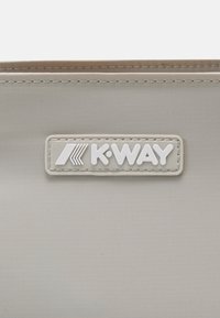 Világosszürke, texturált anyag, amelyen egy fehér K-Way logó címke van rávarrva. Egyszerű, téglalap alakú dizájn, enyhén fénylő felülettel.