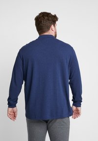 Navyblaue Langarm-Polohemd, weicher Stoff, lockere Passform, mit Kragen und gerippten Bündchen, kombiniert mit grauen strukturierten Hosen.
