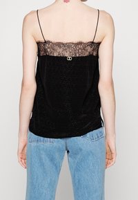 Černá saténová košilka s krajkovým lemem v horní části, vybavená nastavitelnými špagetovými ramínky a zlatým kovovým akcentem na zadní straně.