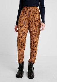 Oranžové kalhoty se vzorem s pružným pasem, s černým potiskem leopardího vzoru, doplněné černými bojovými botami.