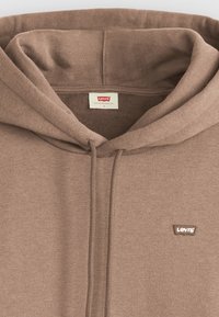 Hnedá mikina s kapucňou vyrobená z mäkkého materiálu, s prednou vreckom, šnúrkou na kapucni a malou nášivkou loga Levi’s na hrudi.