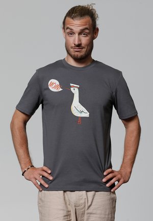 Grijze t-shirt met korte mouwen met een cartoon meeuw en een spraakwolk die "MOIN!" zegt. Het artwork bevat witte, blauwe en rode accenten.