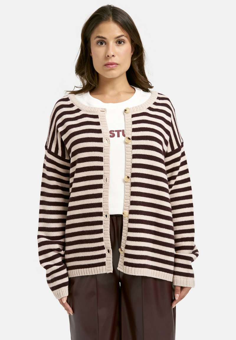 Gestreifter Cardigan in Beige und Dunkelbraun, mit Knopfverschluss vorne, lockeren Ärmeln und geripptem Saum. Über einem weißen Hemd getragen.