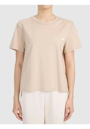 Beżowy t-shirt z krótkim rękawem i okrągłym dekoltem z małym białym logo na piersi, noszony z luźnymi białymi spodniami, pokazany na stojącej osobie.