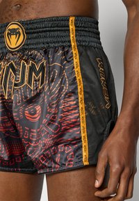 Μαύρο και κόκκινο αθλητικό σορτς με μοτίβο, με ελαστική μέση, που διαθέτει πορτοκαλί λεπτομέρειες και λογότυπο, κατασκευασμένο από ελαφρύ ύφασ μα δίχτυ.