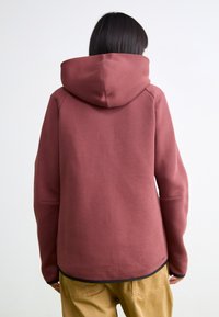Sweatshirt bordô com um grande capuz, feito de um tecido macio. Apresenta um corte descontraído e um design minimalista, sem fechos visíveis.