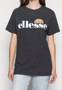 Dark gray cotton t-shirt featuring a white "ellesse" logo and a distinctive orange and red semi-circle graphic above the text. Short sleeves.