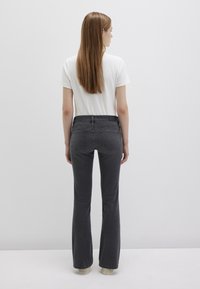 Jeans grigi flared con vita media, dotati di tasche posteriori e una finitura pulita. Abbinati a una maglietta bianca semplice.