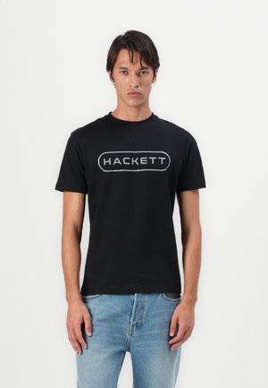 Zwarte katoenen t-shirt met het woord "HACKETT" in een wit ovaal logo. Het shirt heeft een ronde halslijn en korte mouwen.