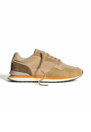 Zapatillas de gamuza color marrón claro con acentos en marrón claro, que cuentan con una mediasuela blanca y una suela negra. Los cordones son de color marrón claro, con una franja naranja en la suela.