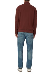 Felpa con zip color marrone scuro e collo alla coreana, abbinata a jeans azzurri a gamba dritta, indossata con sneaker bianche con suola marrone.