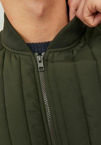 Gestepptes grünes Bomberjackett mit geripptem Kragen, ausgestattet mit einem Frontreißverschluss und strukturiertem Stoff. Nahaufnahme von Kragen- und Reißverschlussdetails.