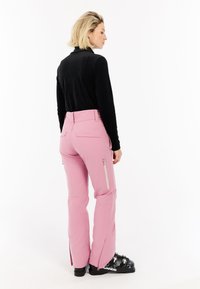 Roze skibroek met ritssluitingen en zips aan de zijkant, gecombineerd met een zwarte aansluitende top. Glad materiaal, tailored fit en functioneel ontwerp.